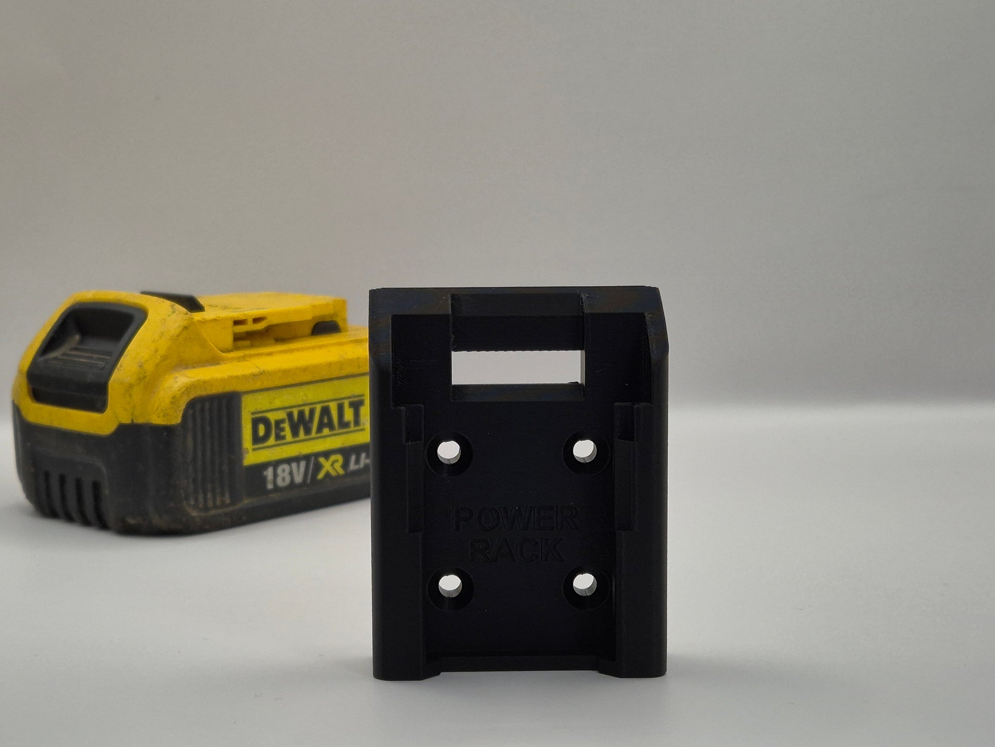 Black Power Rack battery holder next to a yellow and black DEWALT battery on a grey background