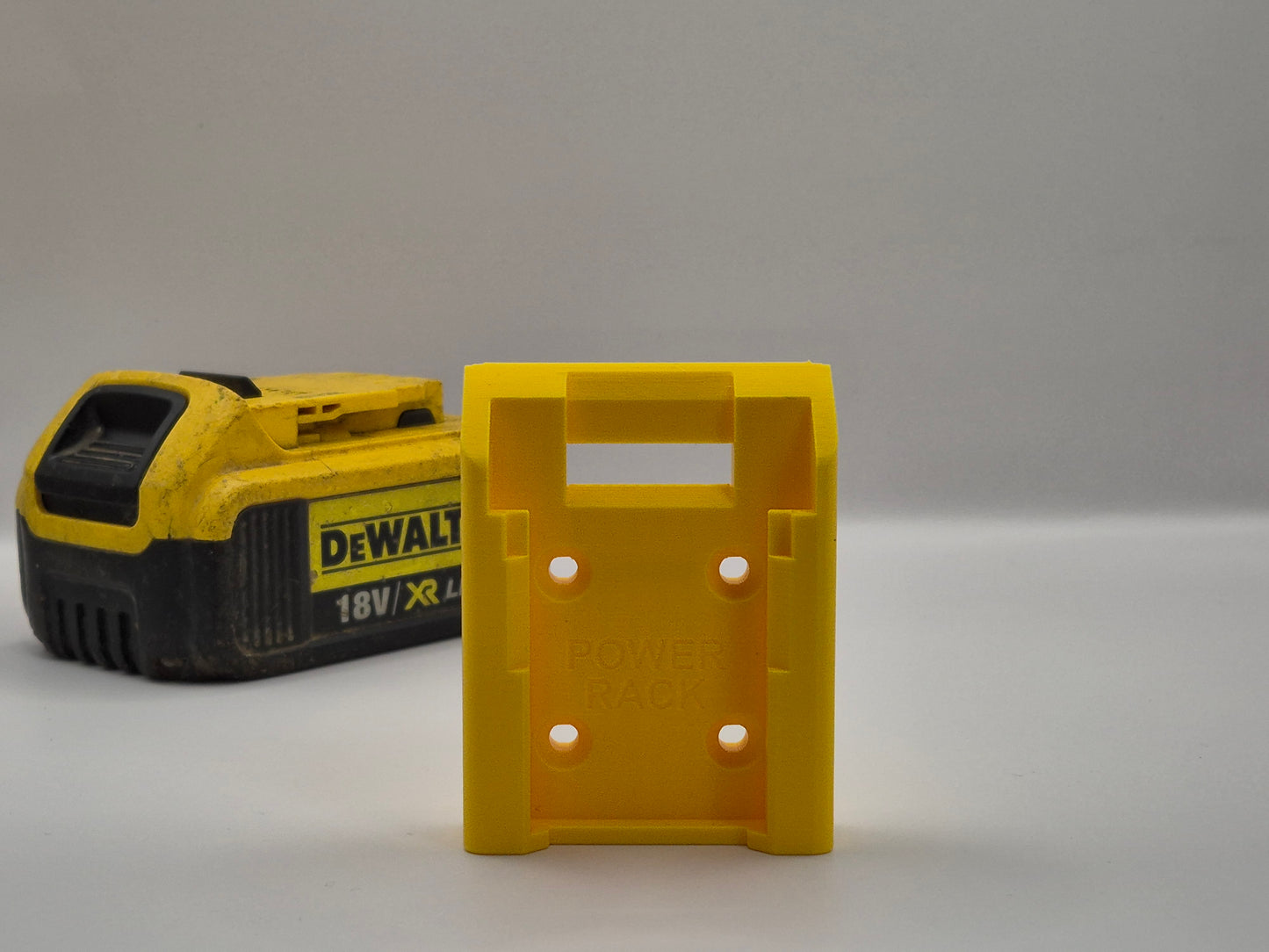 Yellow Power Rack battery holder next to a yellow and black DEWALT battery on a grey background